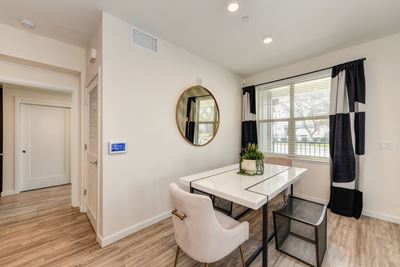 dining area with table, chairs and potted plant on the table. Large window with curtains overlooking the entrance.